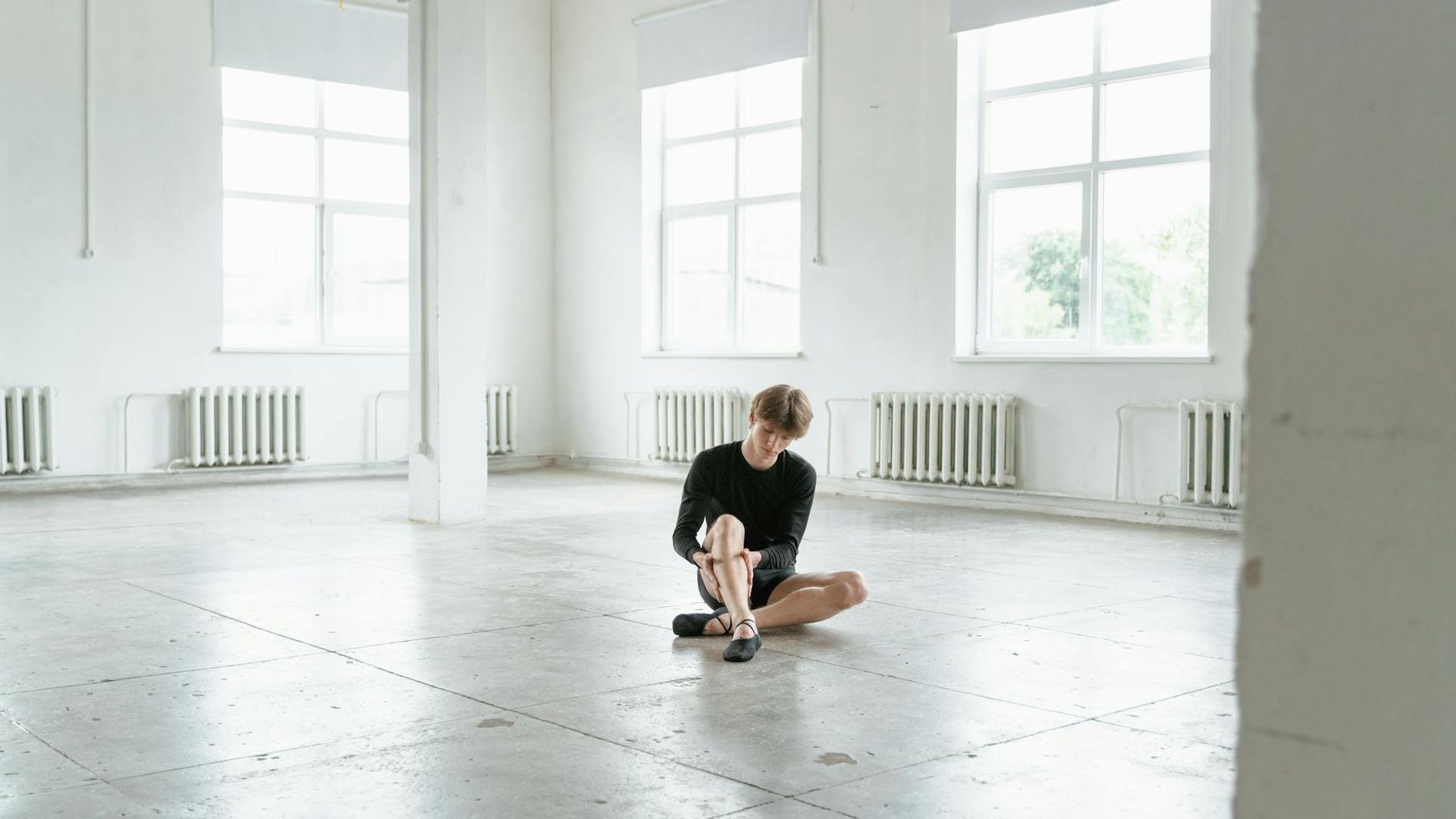 Person practicing slow movements in a dark minimalist studio space.